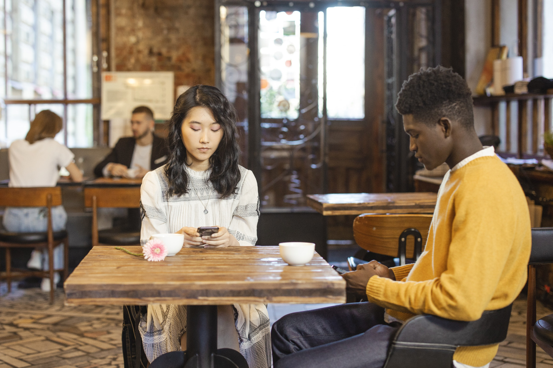 Mixed couple sitting in a restaurant, looking at their phobes and not talking to each other