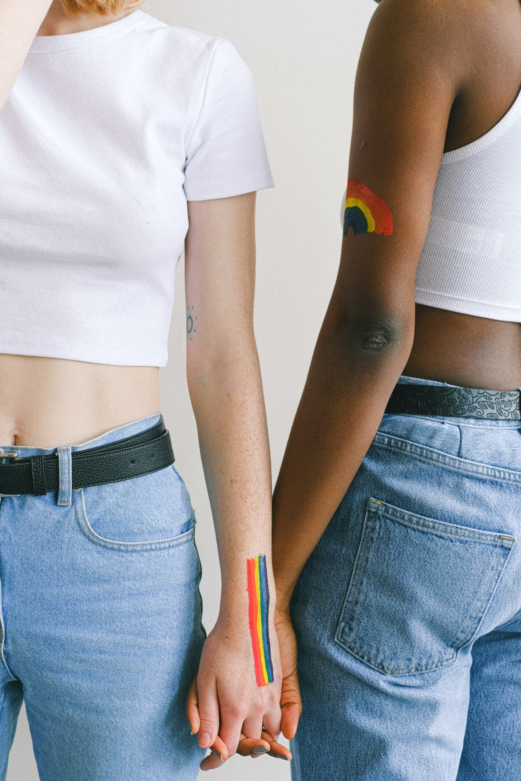 Two women holding hands with a rainbow motif painted on their arms.