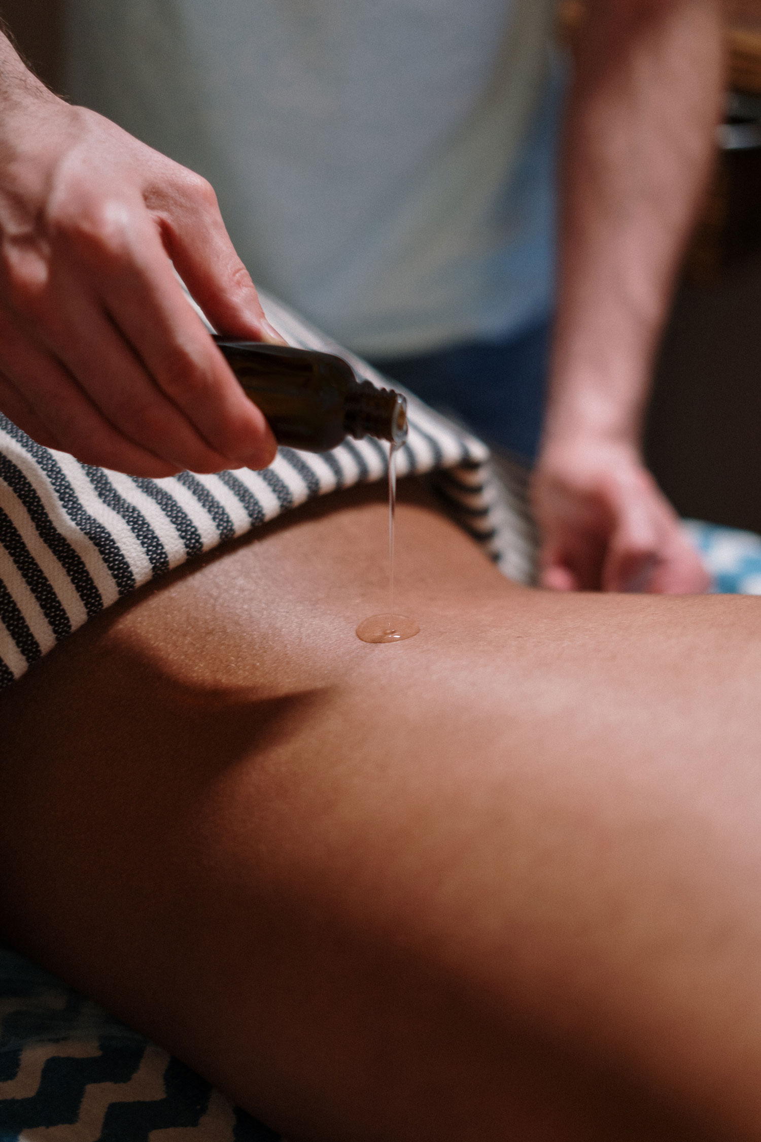 Eine Person träufelt aus einer Flasche etwas Gleitgel auf den Rücken einer anderen Person zur Massage.