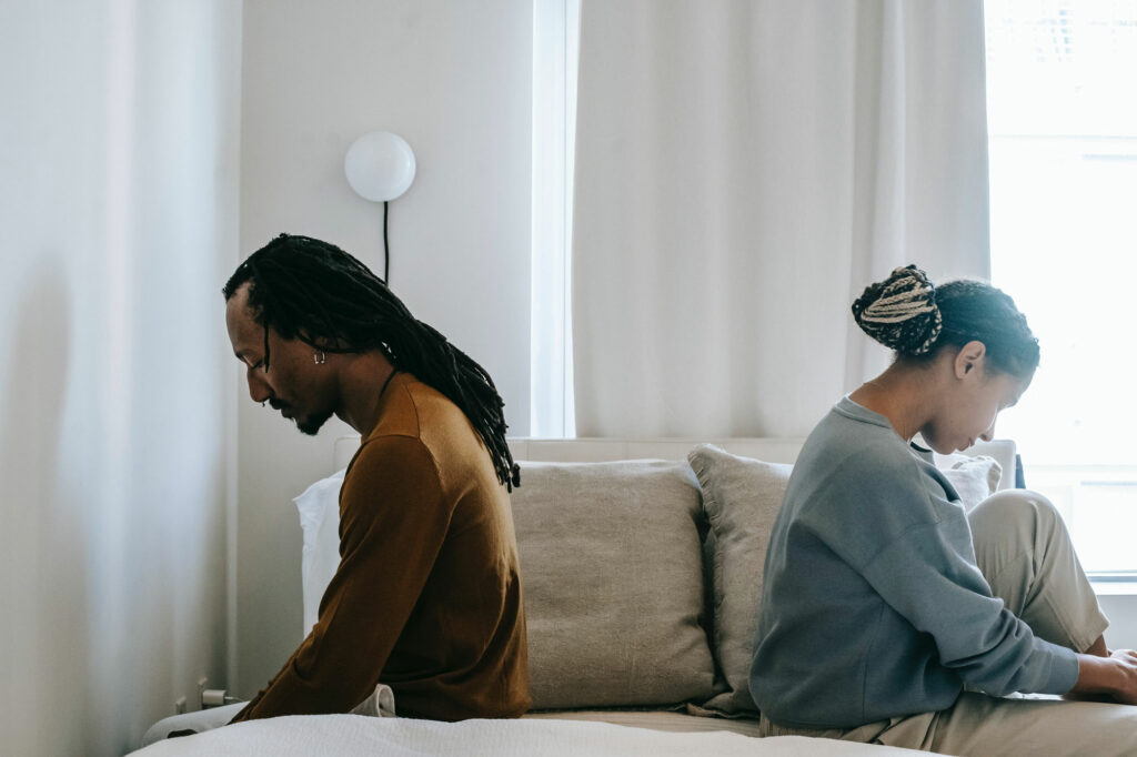 two-people-sitting-sadly-back-to-back-on-bed