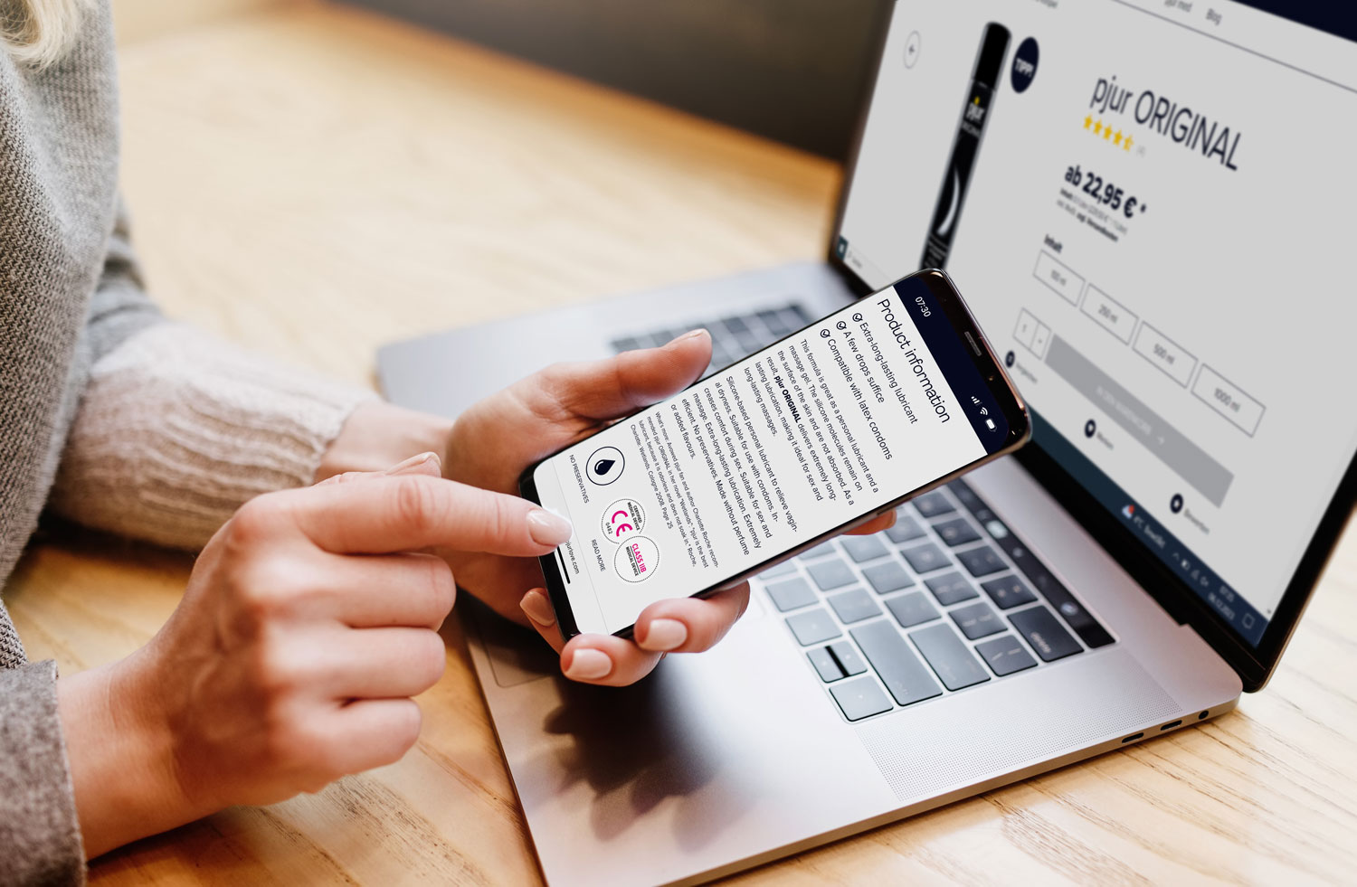 A person is simultaneously researching personal lubricants on their laptop and smartphone in a shop. She taps on her phone screen, accessing product information.