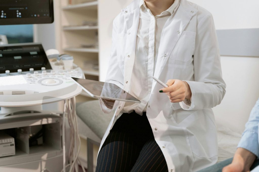 Female doctor holding a tablet and pen, sitting between a patient and a medical device.