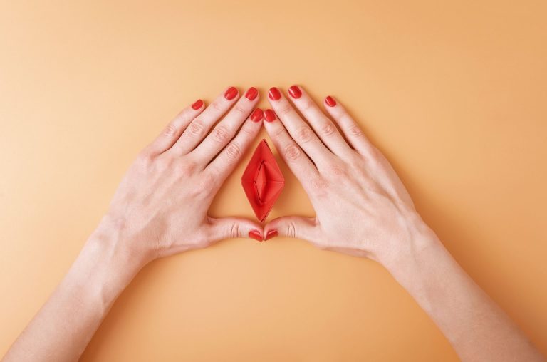 Woman's hands on an orange surface forming a triangle, with a small red origami boat in the center.