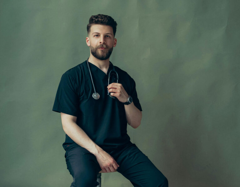 Doctor sitting on a stool with a stethoscope, smiling at the camera.