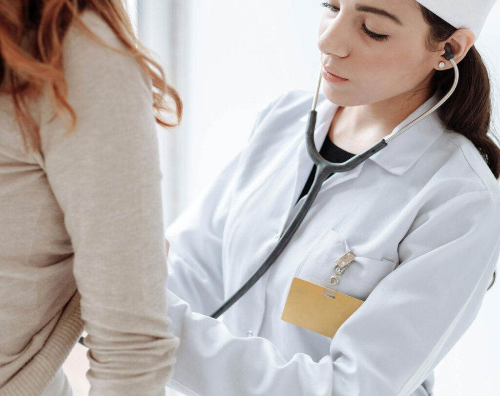 A doctor examines a woman's belly with a stethoscope.